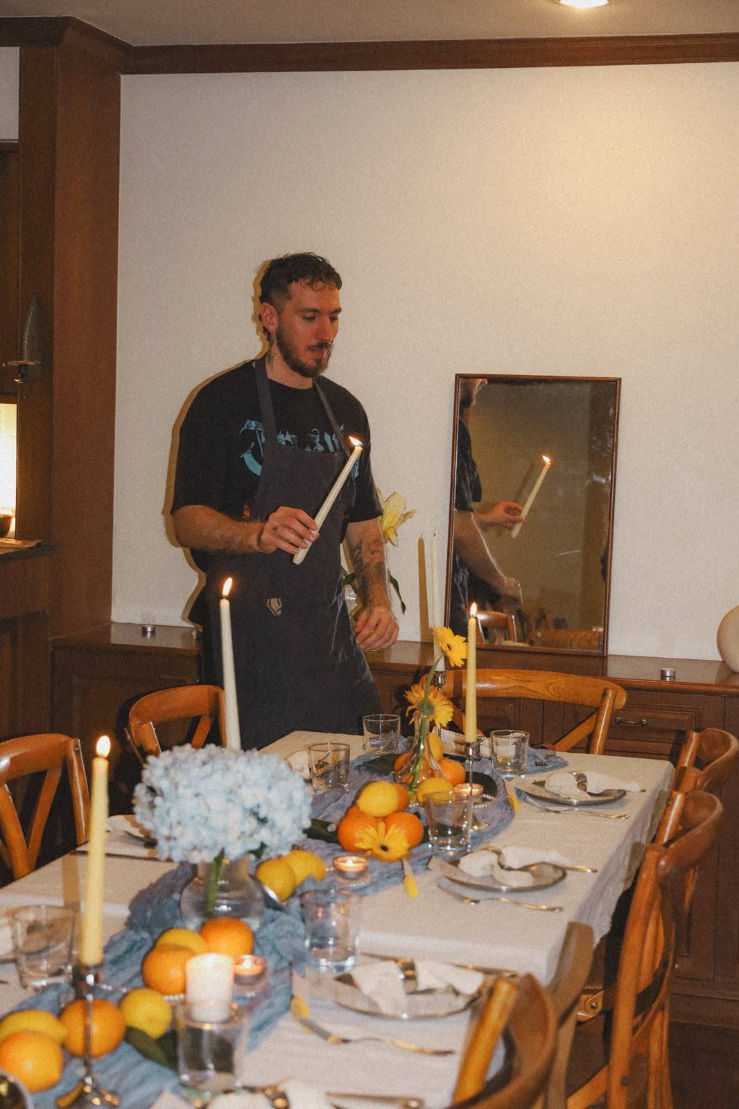 Giuseppe lighting candles on a designed table with citrus and flowers